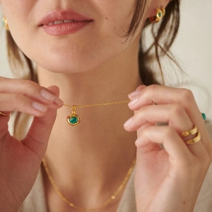 Layered gold necklace set with green oval gemstones and matching rings on a model