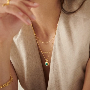 Three-layer gold necklace with round green gemstone pendant on elegant linen clothing