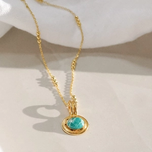 Macro detail of gold layered necklace featuring a round turquoise stone pendant on fine chain