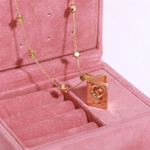 Detailed close-up of a gold book locket necklace with stars on a pink velvet jewelry box