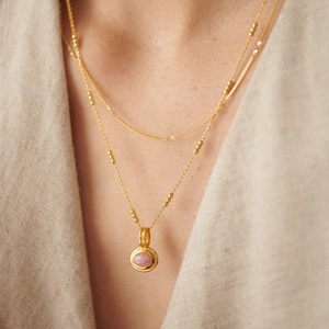 Close-up of double-layer gold plated necklace with pink gemstone pendant on a model