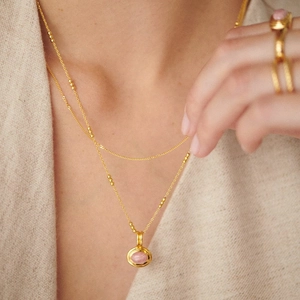 Close-up of double-layered gold necklace with pink oval gemstone on model