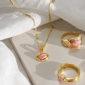 Layered gold necklace and gemstone rings set with pink stones on a stone surface