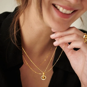 Close-up of layered gold satellite chain necklace featuring a round tiger eye gemstone pendant