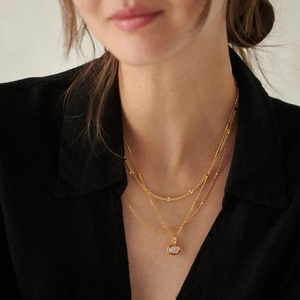 Detailed view of layered gold necklace with pink gemstone pendant on a black shirt