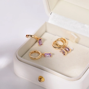 Gold hoop earrings with rectangular purple gemstone in a luxury white jewelry gift box