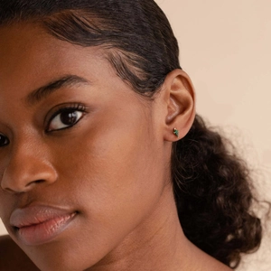 Close-up of a delicate gold-plated emerald stone stud earring worn on a model's ear