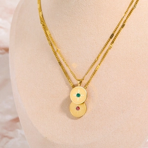 Detail of gold layered necklace featuring emerald and ruby birthstones on starburst pendants