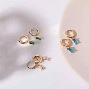 Detailed view of three pairs of gold hoop earrings with emerald, blue, and white stones
