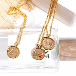 Detailed view of 18K gold zodiac coin pendants with inlaid crystals and a red ruby gemstone