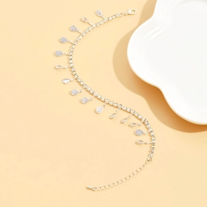 Tobillera de plata con borlas de circón blanco y cristales de gota en fondo beige