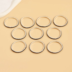Detailed view of ten silver rings set with black zircon stones arranged on a beige background