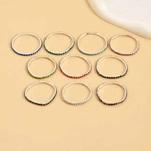 Flat lay of ten silver stretch rings with colorful rhinestones on a beige background