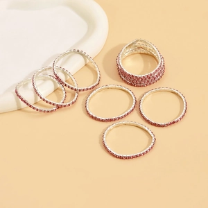 Close-up of sparkling silver rings set with vibrant red and pink crystals on beige surface