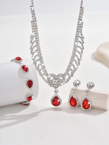 Detailed view of silver necklace and earrings set with red teardrop stones and rhinestones