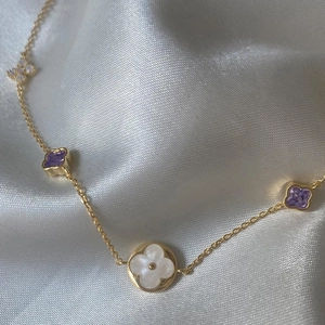 Dettaglio collana in oro 18K con ciondoli a quadrifoglio viola su seta bianca