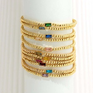 Close-up of gold beaded bracelets with multi-color rectangular gemstone inlays