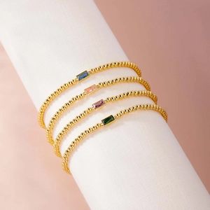 Close-up of four gold bead bracelets with colorful rectangular step-cut gemstones