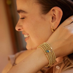 Detail of layered gold beaded bracelets with colorful birthstones and twisted hoop earring