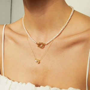 Detalle de collares dorados a capas con gargantilla de perlas y colgante de gota de circón