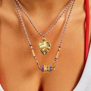 Primer plano de collares trenzados en capas con colgante de corazón dorado y dije esmaltado