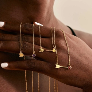 Detail view of heart-shaped birthstone necklaces on hand with elegant gold arrows