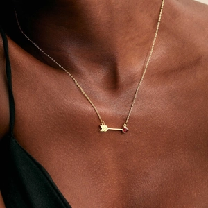 Detail of 18K gold birthstone necklace with red heart arrow pendant on model's neckline