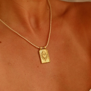 Detailed macro of gold Sacred Heart tarot pendant on white and gold braided cord