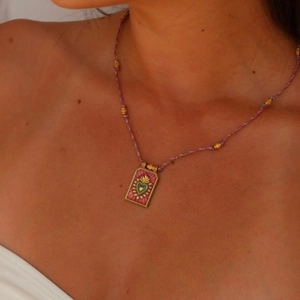Close-up of a vintage-style gold tarot heart pendant on a pink braided cord necklace
