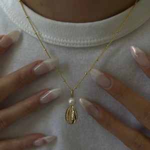 Detail view of a shell and pearl necklace on a neck with a golden bead chain