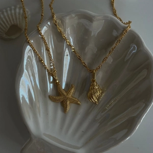 Detail of gold starfish and conch shell pendants on an elegant white nautical tray