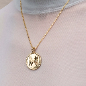 Macro di un ciondolo a moneta dorata con mani in rilievo su una collana a maglie fini