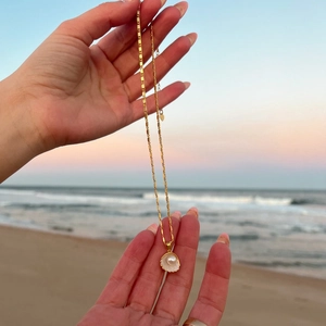 Detail of gold seashell necklace with pearl on sunset beach background with ocean waves