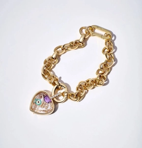 Macro view of golden link bracelet with a heart locket featuring blue eye and crystal charms