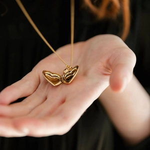Gros plan du collier médaillon en forme de cœur doré tenu à la main montrant les détails