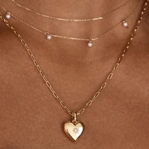 Detail of layered gold heart locket necklace with white pearls and paperclip chain