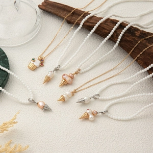 Macro detail of pearl chain necklaces with ice cream and cupcake pendants on white stone