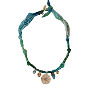 Detail of silk cord necklace with gold sun charms, evil eye, and green gemstone pendants