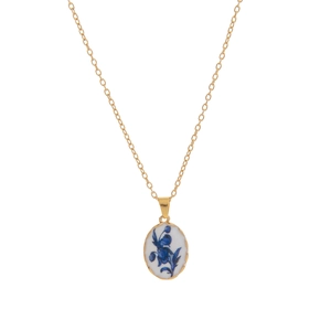 Close-up of oval white porcelain pendant with vintage blue floral patterns on gold chain