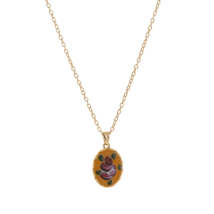 Macro shot of gold oval pendant featuring vintage rose floral pattern on yellow background