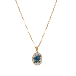 Close-up of vintage oval gold necklace with blue rose floral pattern on white enamel