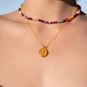 Close-up of stacked evil eye necklaces with colorful beads and gold 18k plated pendant