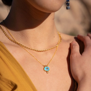 Close-up of layered 18k gold plated evil eye pendant necklace worn by a fashion model