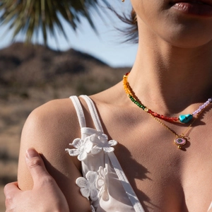 Close-up of layered necklace with colorful beads and a pink evil eye pendant on a model