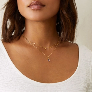 Close-up of double layer gold necklace featuring a purple marquise gemstone pendant