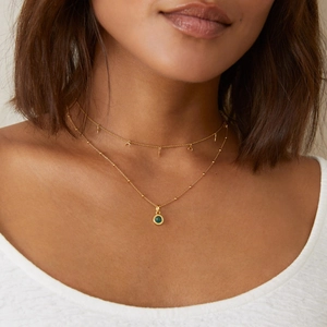 Close-up of layered 18K gold plated necklace with moon charms and green gemstone pendant