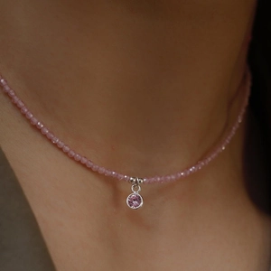 Dettaglio collana di perline rosa con ciondolo in zircone argento indossata al collo