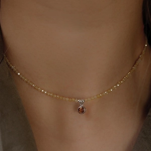 Dettaglio di collana con perline gialle e ciondolo gemma rossa indossata sulla clavicola