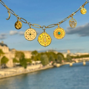 Close-up of golden zodiac necklace with turquoise sun and moon charms against a blue sky