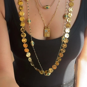 Detail view of layered gold necklaces featuring evil eye pendant and green stone beads